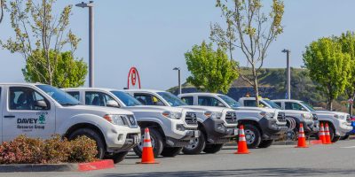 Fleet of utility trucks parked in an outdoor lot with safety cones and trees.