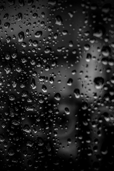 Close-up of raindrops on a glass surface with a dark background, creating an abstract and moody effect.