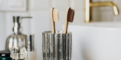 Eco friendly bamboo toothbrushes in silver glass placed in bathroom near sink and beauty products
