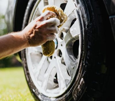 Close-up of a person washing a car tire with foam and sponge outdoors.